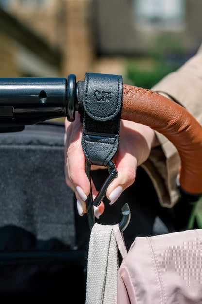 Hand holding a stroller handle with a close-up of the hand and stroller, blurred background
Close-up of Harper & Me buggy clips securing shopping bags to pushchair
