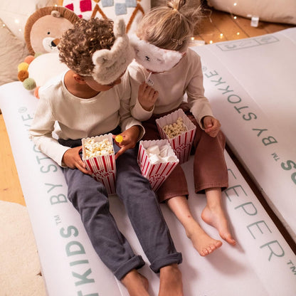 Two children sat on a cloud sleeper eating popcorn 