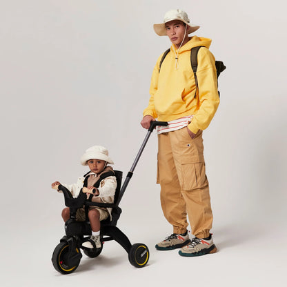 Toddler riding the Doona Liki Trike S5 in Midnight Black with extended sunshade and secure harness — rent now from Thursday’s Child.